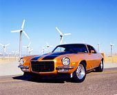 CAM 04 RK0069 03
1973 Chevrolet Camaro Gold Black Stripe Low 3/4 Front View On Road By Wind Turbines