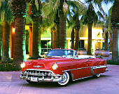 AUT 21 RK0126 01
1953 Red Chevy Bel Air Convertible Custom 3/4 Front On Pavement By Palm Trees & Building At Dusk Headlights On