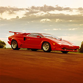 LAM 01 RK0160 02
1989 Lamborghini Countach 25th Anniversary Red 3/4 Front View On Pavement Headlights On Sunset Clouds