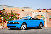 MST 01 RK1248 01
2011 Ford Mustang GT Blue 3/4 Side View On Pavement By Painted Wall With Red Flowers