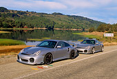 POR 04 RK0562 08
2004 X50 And 2002 996 Turbo Silver 3/4 Front View On Road By Water And Trees