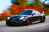 POR 04 RK0795 01
2008 Porsche Cayman S TechArt Black 3/4 Front View Driving By Foliage