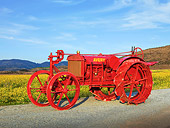 TRA 01 RK0141 01
1918 Avery Model B Tractor Orange 3/4 Side View On Gravel By Field Of Wildflowers