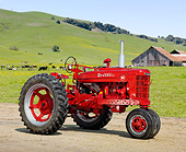 TRA 01 RK0206 01
1950 Farmall M Tractor Red 3/4 Side View On Dirt By Grassy Hills And Cows